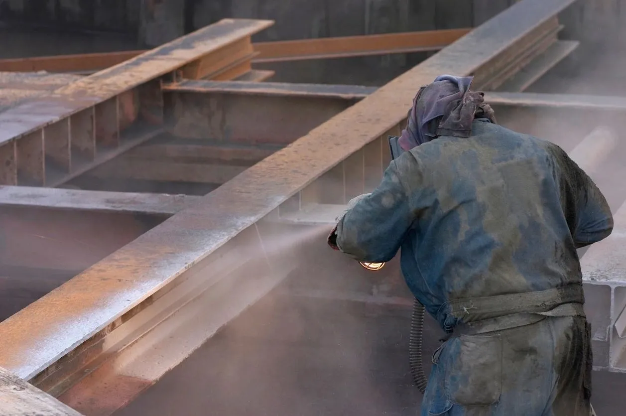 A person in blue coveralls and white gloves using an air gun.