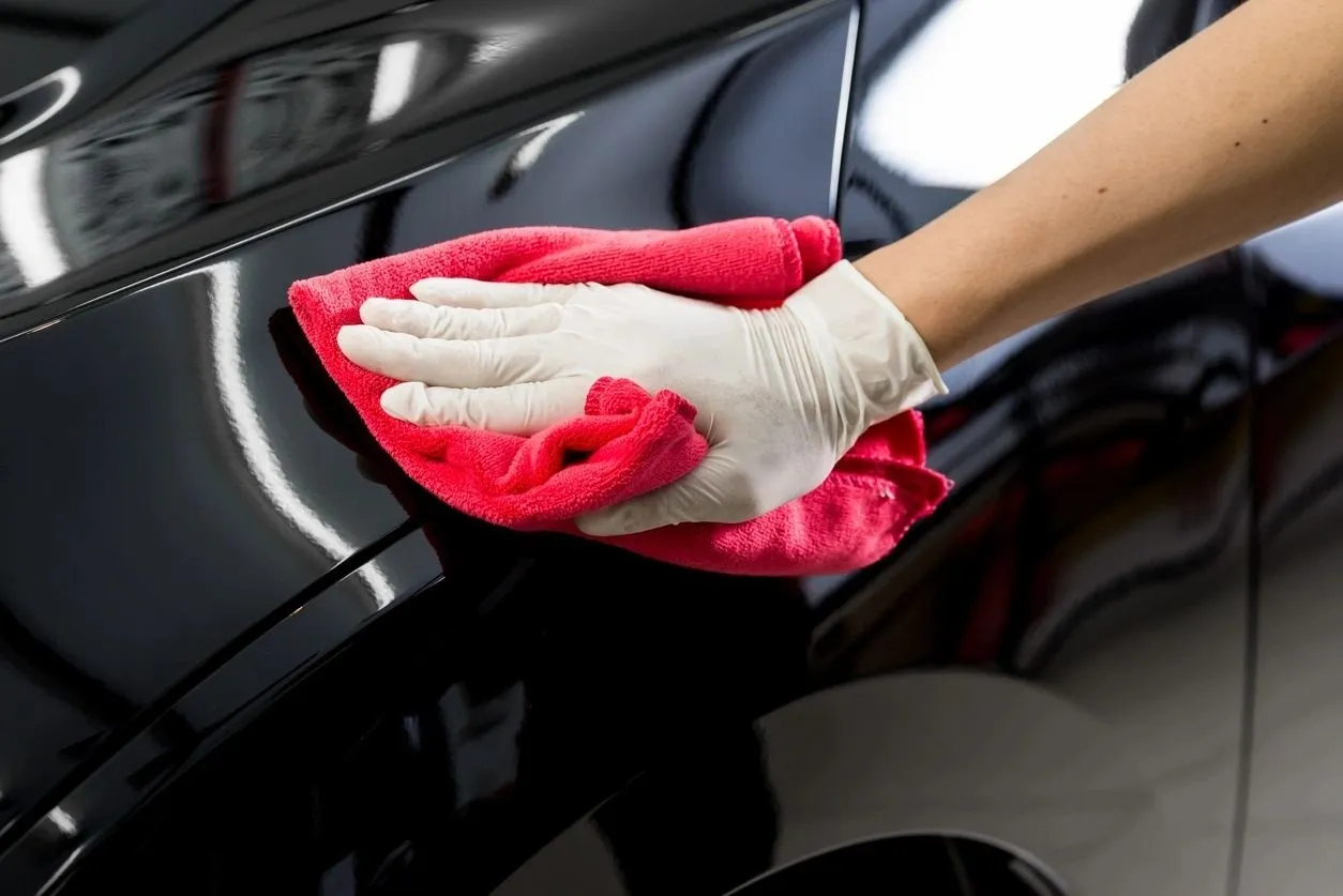 A person cleaning the side of a car with red cloth.