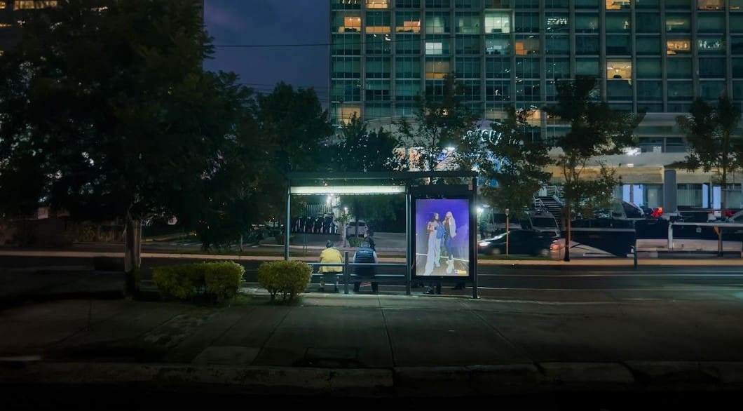 A bus stop with people standing at the side of it.